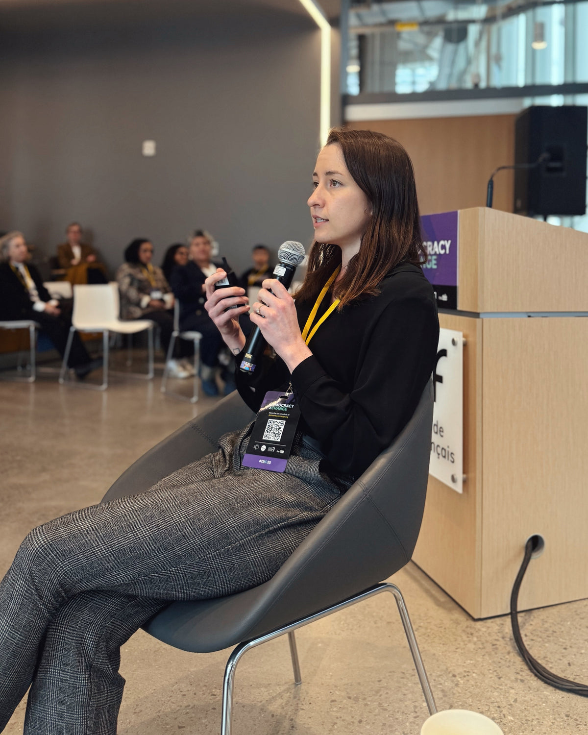 Emma Cochrane speaking into a microphone at DemocracyXChange 2025 in Toronto